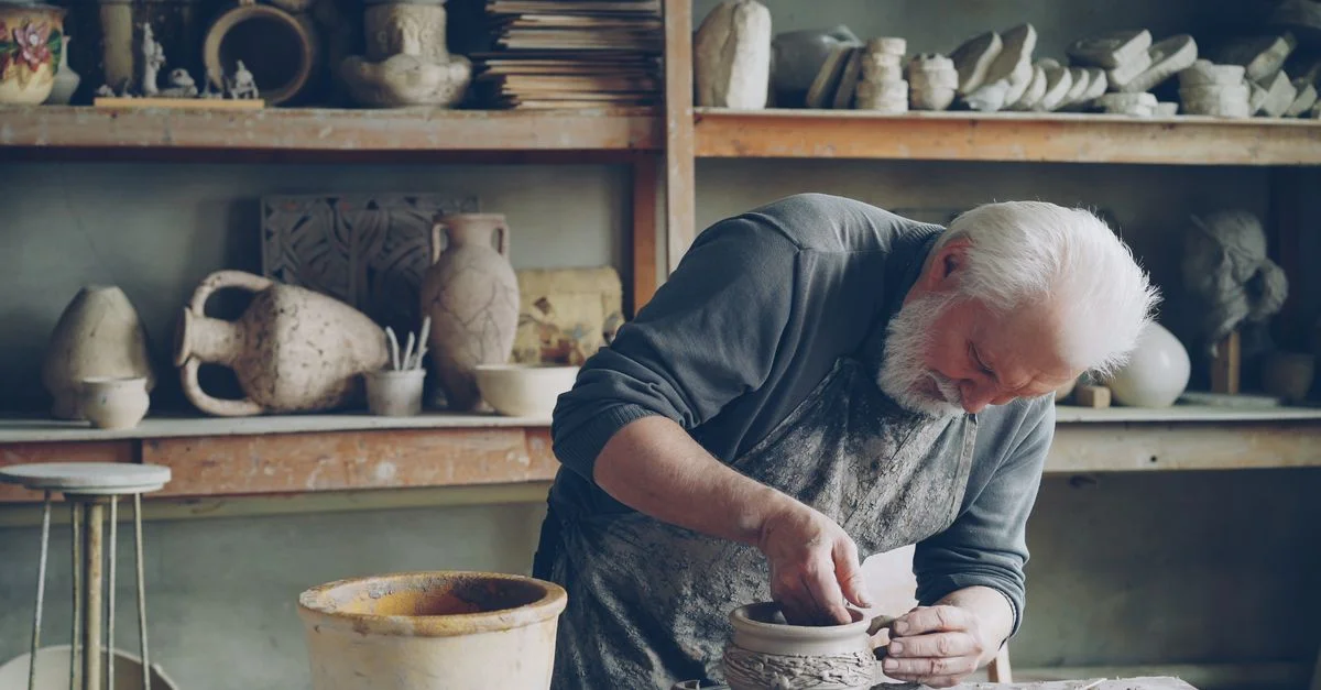 Un artisan senior façonne de l'argile en grès dans un atelier de poterie rustique. Scène de créativité et d'artisanat.