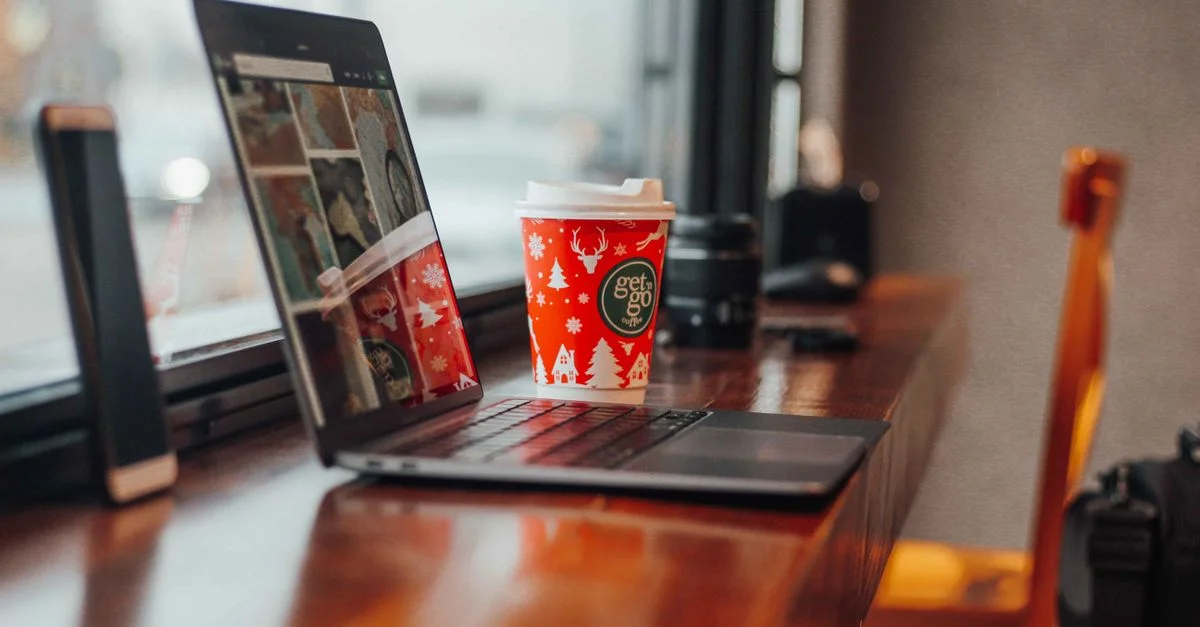 Scène intérieure chaleureuse avec un ordinateur portable et une tasse de café sur le thème de Noël sur une table en bois.