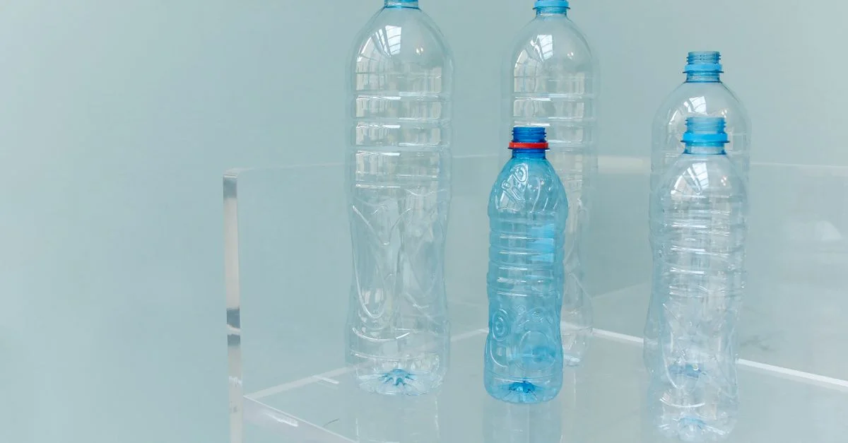 Cinq bouteilles en plastique vides assorties exposées sur une étagère transparente avec un fond bleu doux.