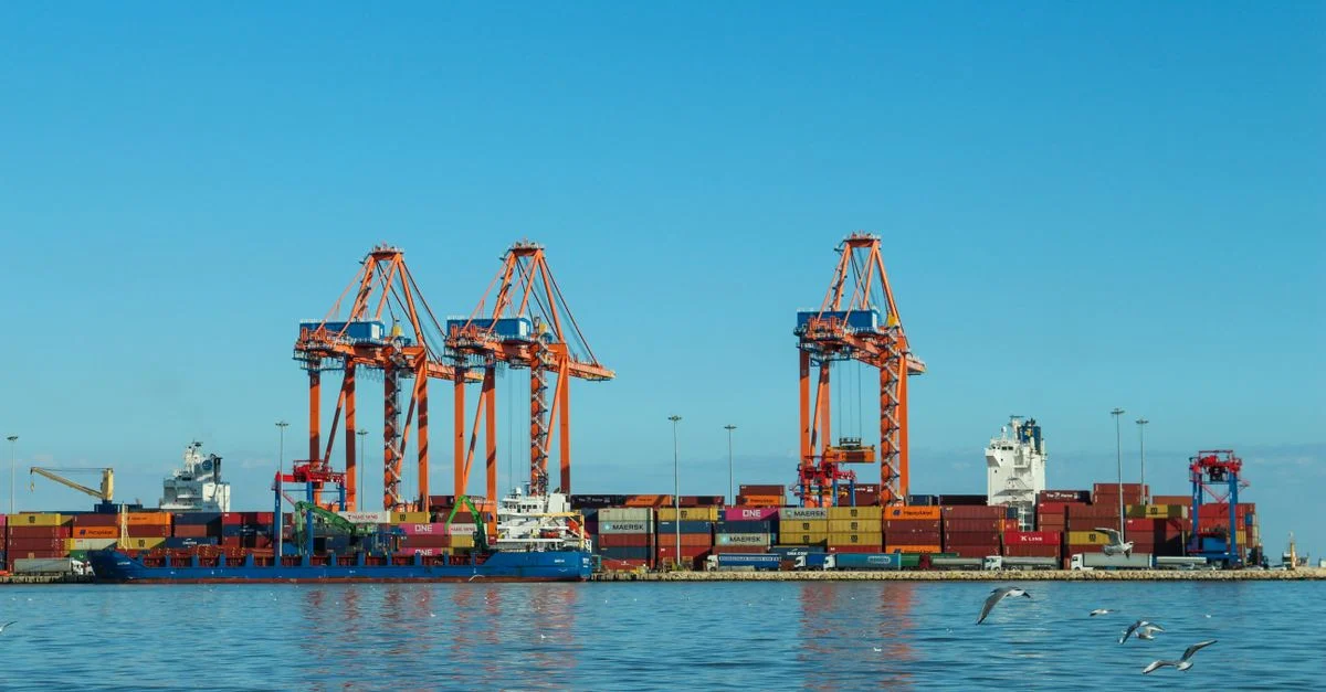 Port à conteneurs coloré avec de grandes grues et des navires contre un ciel bleu clair.