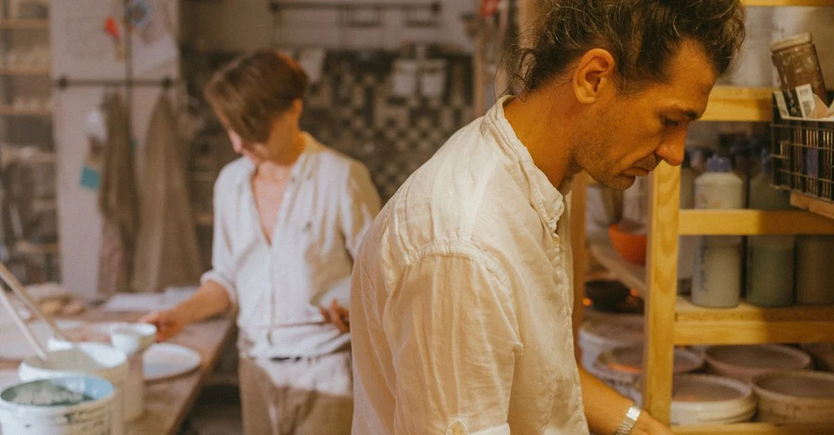 Deux artistes céramistes concentrés sur leur travail dans un studio de poterie, mettant en valeur leur créativité.